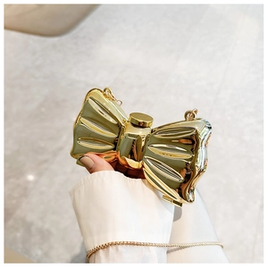 Close-up of a golden bow-shaped evening bag with a metallic mirror finish and thin chain