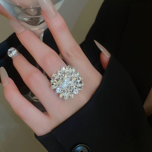 Detailed view of a sparkling crystal flower ring worn on hand holding a glass