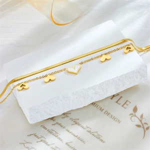 Detail of golden double-layer anklet featuring white shell heart charm and snake chain