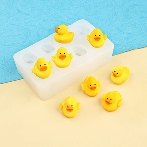 White silicone 8-cavity mini duck mold with yellow resin ducklings on a blue background