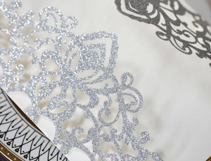 Macro view of laser-cut glitter paper card featuring intricate silver floral patterns