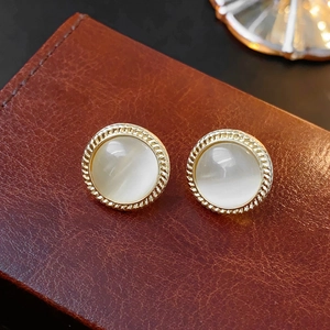Close-up of vintage gold round stud earrings with white cat-eye stone on leather background