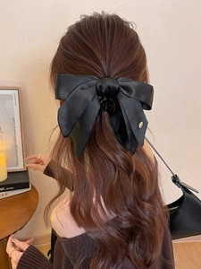 Detail of a black satin bow hair claw clip with golden metal accent on wavy brown hair