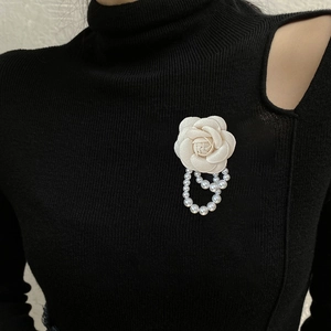 Detailed shot of camellia flower brooch with pearl tassel on black knit garment