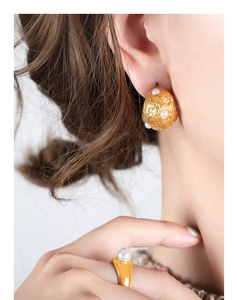 Dettaglio di orecchini vintage dorati e un anello con perla su una modella
