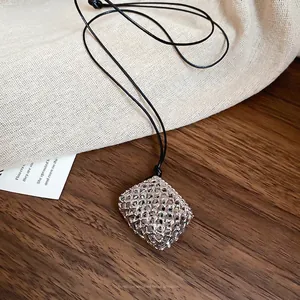 Minimalist wax cord necklace with a silver hollow cube pendant on a rustic wooden background