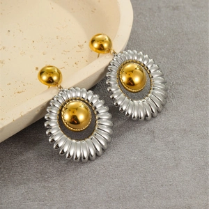 Close-up of two-tone geometric drop earrings with gold and silver spheres on stone tray