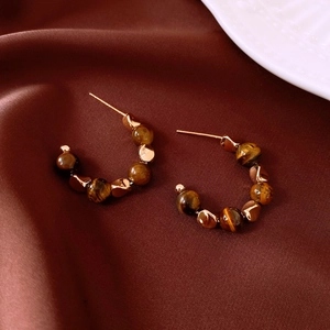 Detail of C-shaped 18k gold plated tiger eye stone earrings on dark brown silk fabric