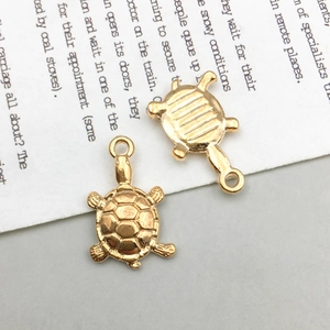 Detailed view of two golden sea turtle alloy pendants for DIY jewelry on vintage paper