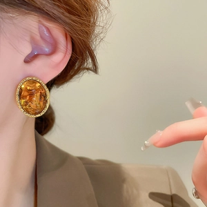 Close-up of amber resin earring with textured gold metal edge worn by a model