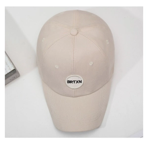 Detailed close-up of light beige baseball cap with BRTXN embroidery and vent holes