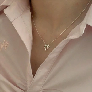 Close-up of a silver bow pendant necklace worn by a model against a soft pink shirt