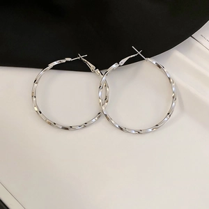 Detail of silver twisted hoop earrings with a metallic spiral design on a dual-tone background