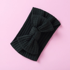 Detailed close-up of a black waffle knit baby headband with a large bow on pink background