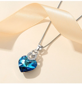 Detailed view of heart-shaped blue crystal pendant with silver box chain and satin ribbon