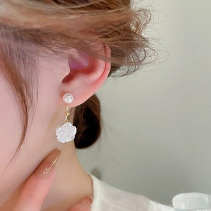 Close-up of elegant white flower pearl earrings worn by a model in soft natural light