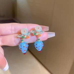 Macro view of blue strawberry earrings with green leaf details and white bead accents