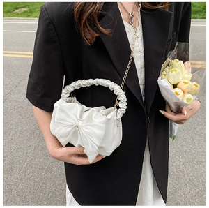 Detail of white pleated cloud bag with large bow decoration and golden chain strap