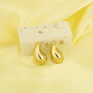 Detailed view of polished 18K gold teardrop earrings on a minimalist stone display
