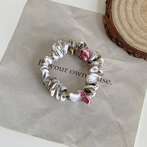 Close-up of silk floral scrunchie with pink and green flower patterns on white background