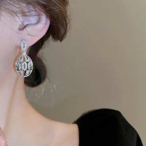 Close-up of silver oval hoop earrings with white zircon and green gemstone accents