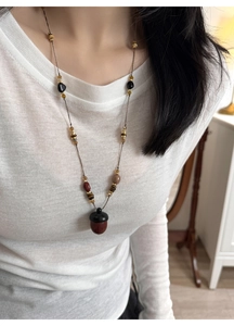 Detail of a retro long beaded necklace featuring a bicolored wooden acorn pendant on a model