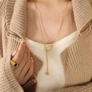 Gold-plated Y-necklace with sphere pendant and emerald-style gemstone ring worn on knitwear