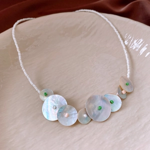 Detail of round shell and rose quartz pendant necklace on a ceramic jewelry tray