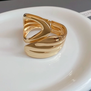 Detailed view of wide gold wave bangle with sculptural texture on white ceramic plate