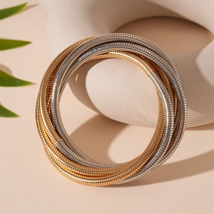 Detail von mehrlagigen Schlangenknochen-Armbändern in Gold und Silber auf Keramik