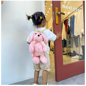 Detail view of pink plush cartoon dog backpack with beige straps on child model
