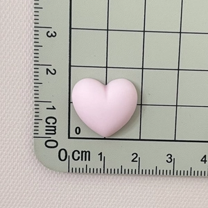 Close-up of pink matte resin heart charm measuring 1.5 cm on a green grid ruler