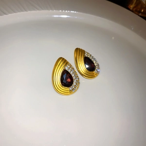 Close-up of golden teardrop earrings with red gemstone and white crystals on ceramic