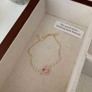 Dettaglio del bracciale con perle dorate e ciondolo a pesca in una scatola di legno