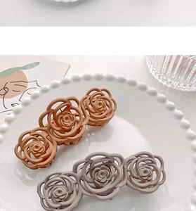 Detail of two matte hollow camellia hair claws in caramel and taupe on a white plate