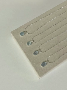 Detailed view of four natural aquamarine oval pendants on silver chains over grey velvet