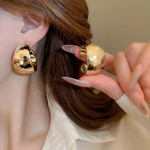 Detail of chunky gold C-shaped earrings featuring a vintage hammered metal texture surface