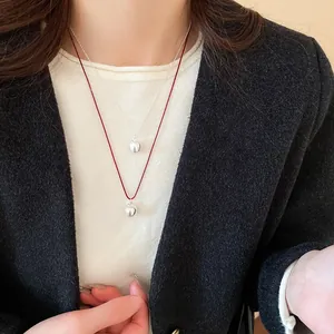 Detail of red cord and silver apple pendant necklace worn over a black tweed jacket