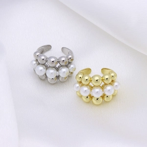 Macro detail of elegant layered pearl rings with metallic spheres on white fabric
