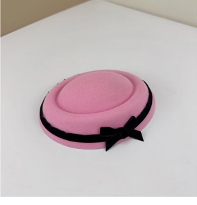 Detail of pink wool pillbox hat featuring a black velvet ribbon and elegant side bow accent