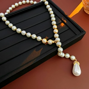 Detail view of water-drop pearl pendant with gold setting on luxury beaded necklace