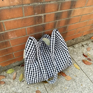 Detail of black and white checkered canvas tote bag with woven label on brick wall background
