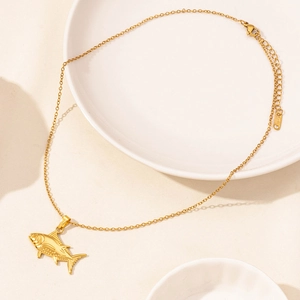 Detailed view of golden fish pendant on O-chain necklace resting on a ceramic dish