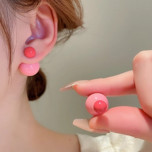 Detail of red and pink double ball resin stud earrings shown on ear for layering effect