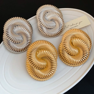 Macro detail of gold and silver textured spiral earrings on white ceramic tray