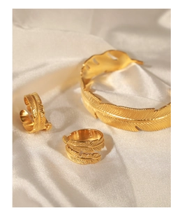 Detail of golden feather jewelry set including bracelet and rings on white silk fabric