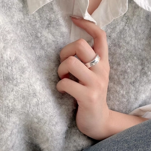 Detail of a minimalist wavy sterling silver ring worn over a white shirt and knit sweater