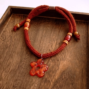 Detailed view of red resin flower pendant and braided cord on a dark wooden tray