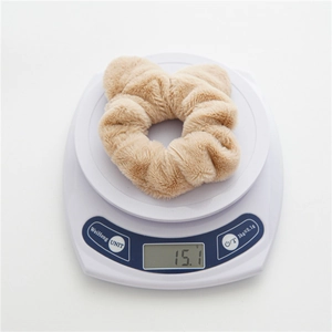 Detailed view of beige plush scrunchie on electronic scale showing 15.1g lightweight