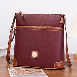 Detail of burgundy pebble leather crossbody bag with brown trim on a wooden table